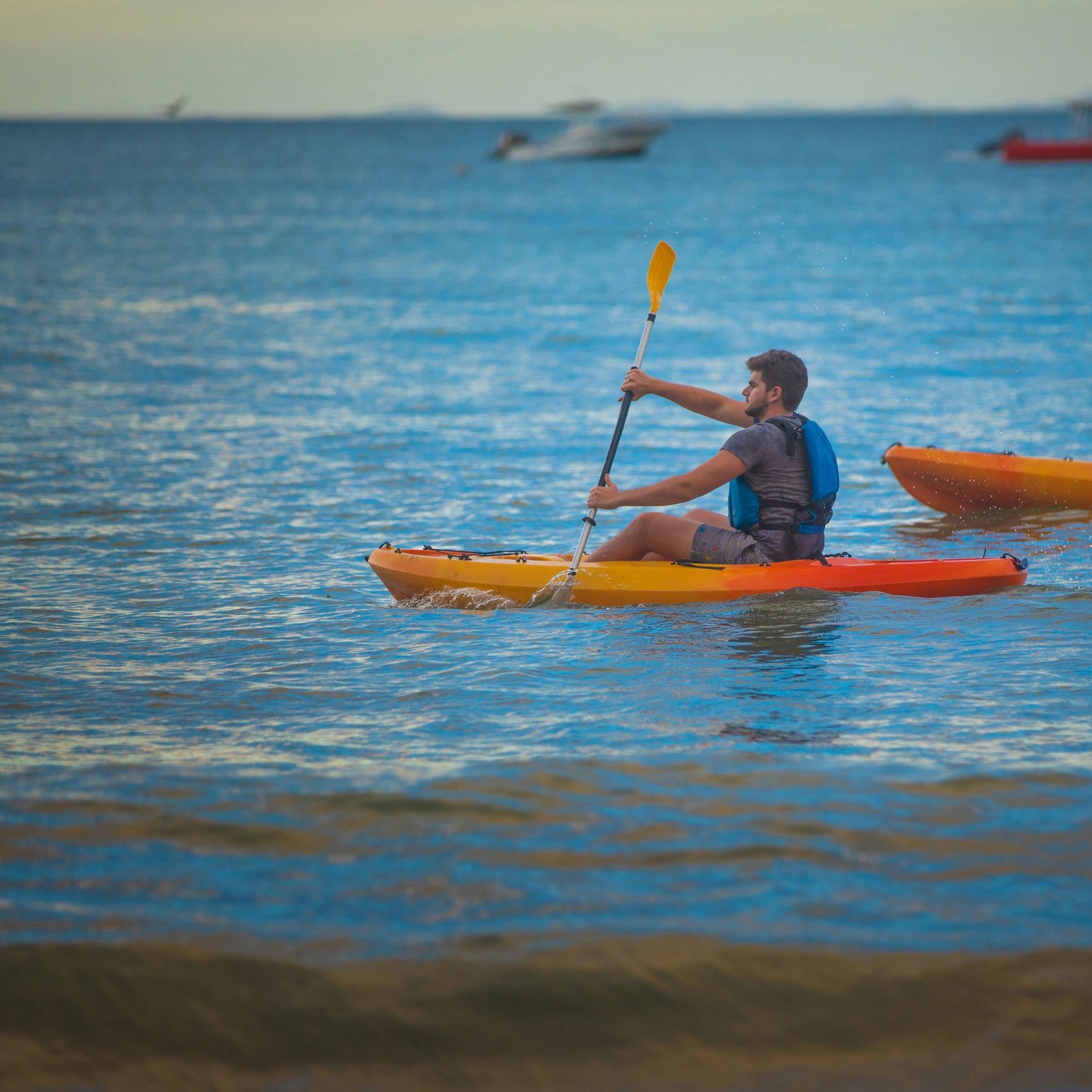 Man paddling a yellow kayak in coastal water